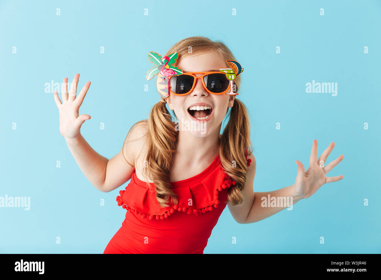 Cheerful little girl wearing swimsuit standing isolated over blue ...