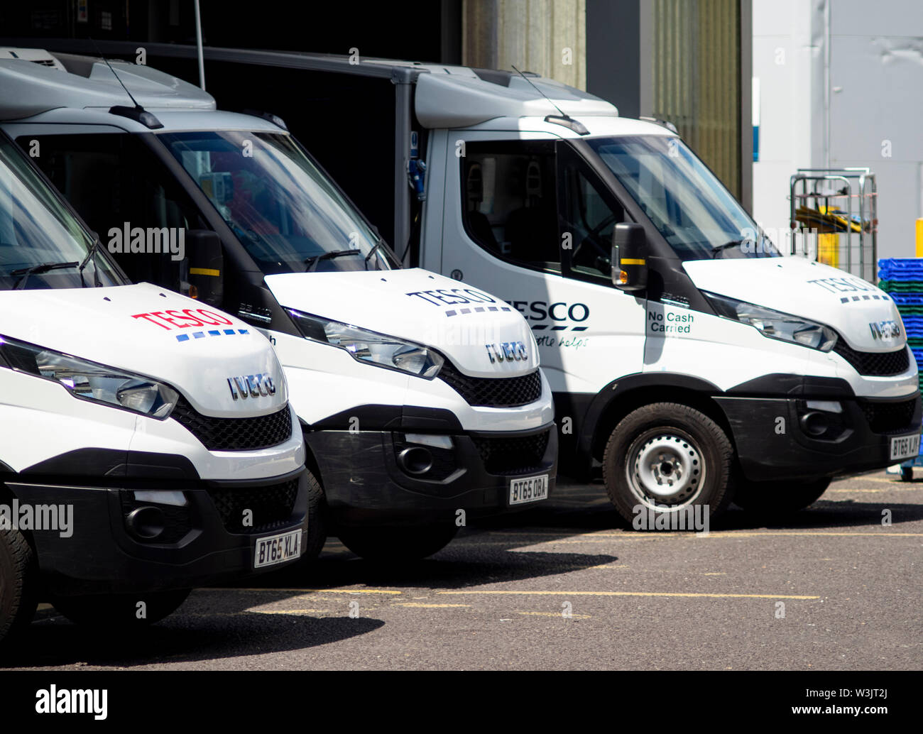 A line of stationary Tesco home delivery vans in diminishing perspective in their loading bays waiting to be loaded before going out on their routes. Stock Photo