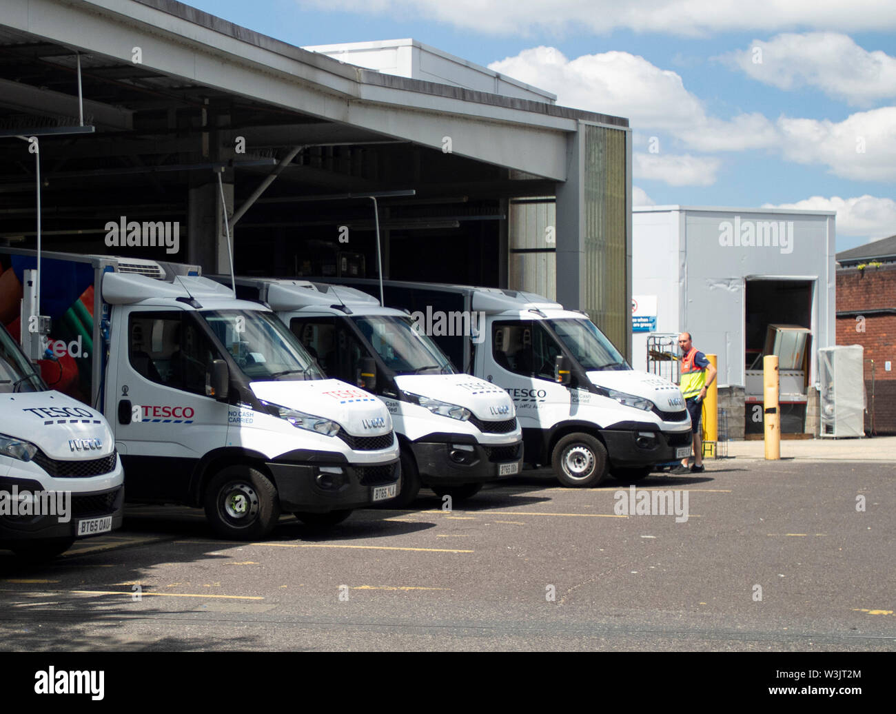 A line of stationary Tesco home delivery vans in diminishing perspective in their loading bays waiting to be loaded before going out on their routes. Stock Photo