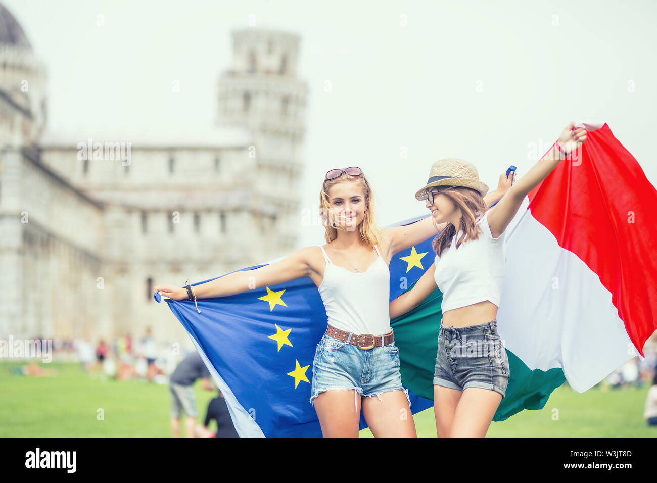 Young teen girls traveler with italian and european union flags  before the historic tower in town Pisa - Italy. Stock Photo