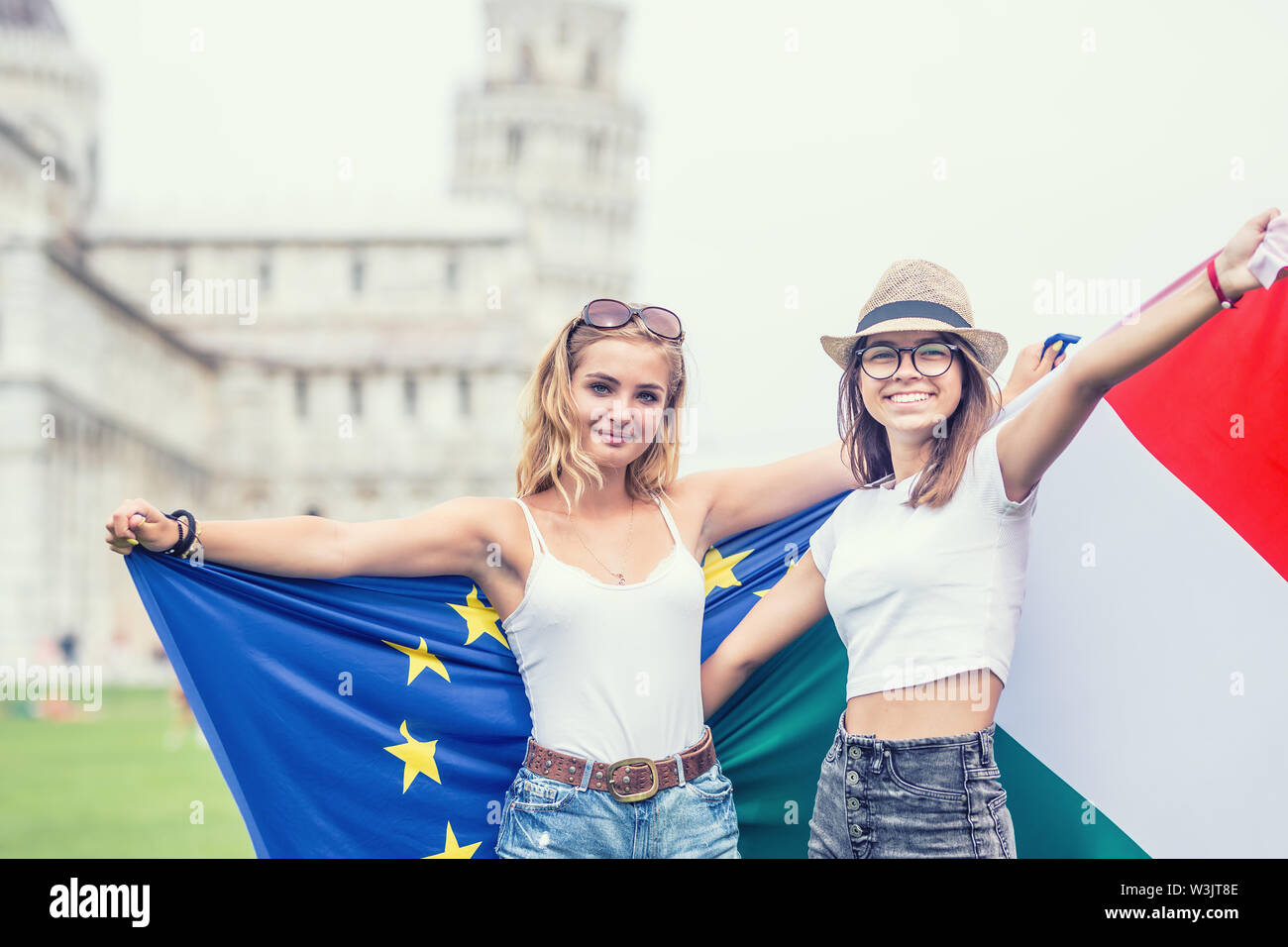 Young teen girls traveler with italian and european union flags  before the historic tower in town Pisa - Italy. Stock Photo