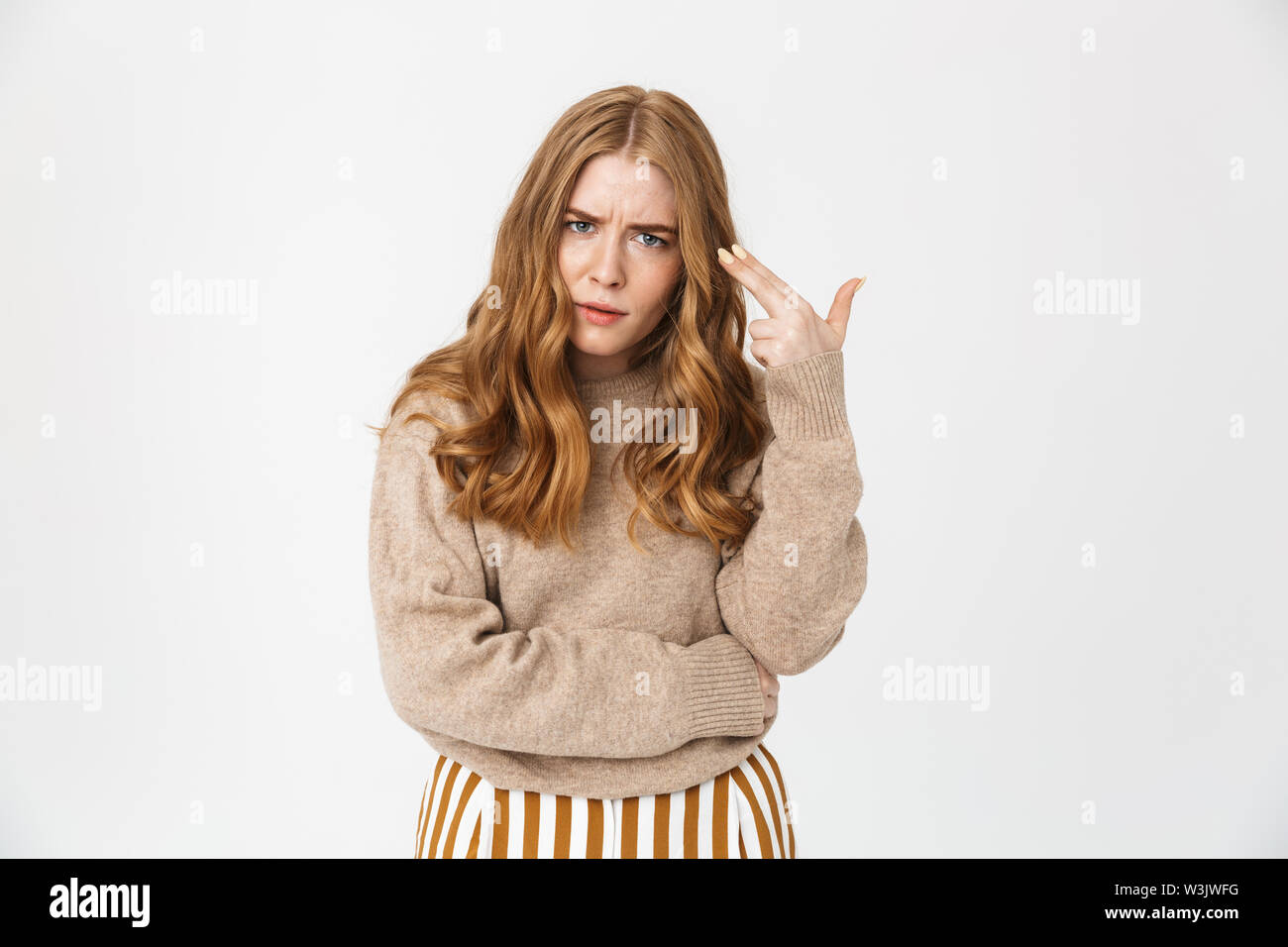 Attractive young girl wearing sweater standing isolated over white background, holding pretend gun at her head Stock Photo