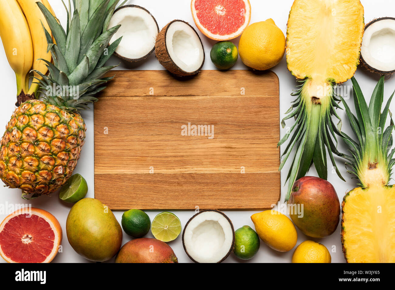 top view of cut and whole tropical fruits around wooden chopping board ...