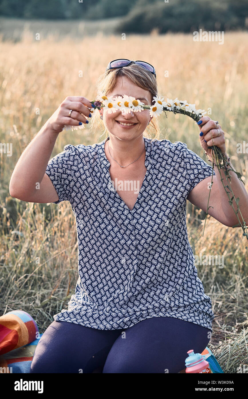 Smiling happy woman making coronet of wild flowers. Family spending time together on a meadow, close to nature. Candid people, real moments, authentic Stock Photo