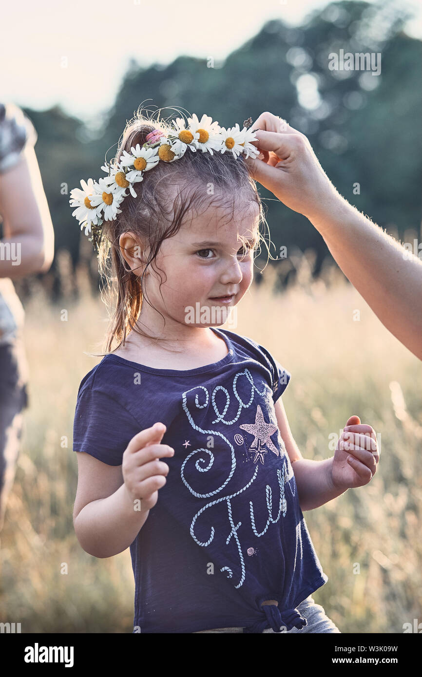 Mother putting a coronet of wild flowers on a head of little girl. Family spending time together on a meadow, close to nature. Parents and children pl Stock Photo