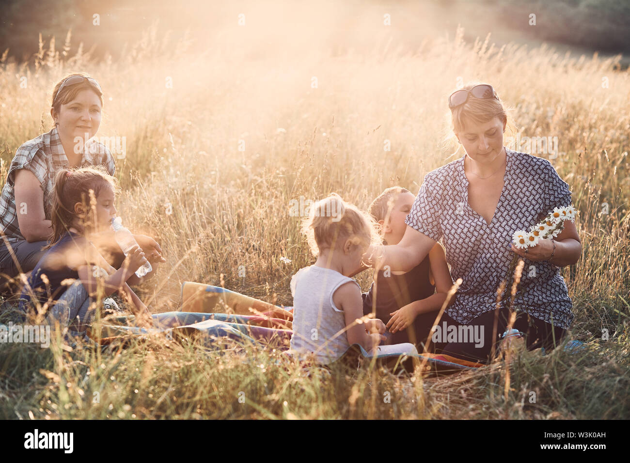 Family spending time together on a meadow, close to nature, parents and children playing together, making coronet of wild flowers. Candid people, real Stock Photo