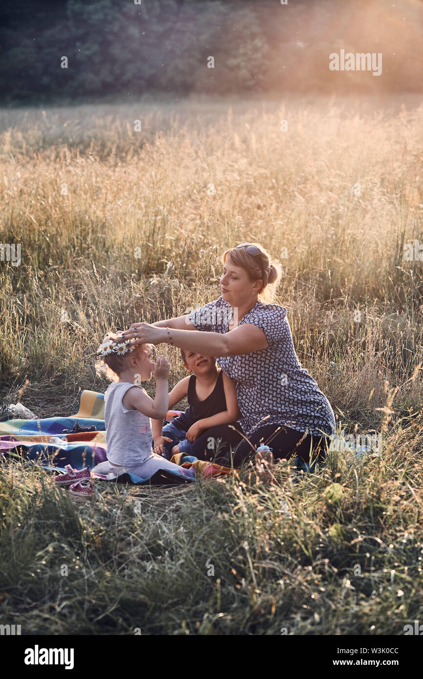 Family spending time together on a meadow, close to nature, parents and children playing together, making coronet of wild flowers. Candid people, real Stock Photo
