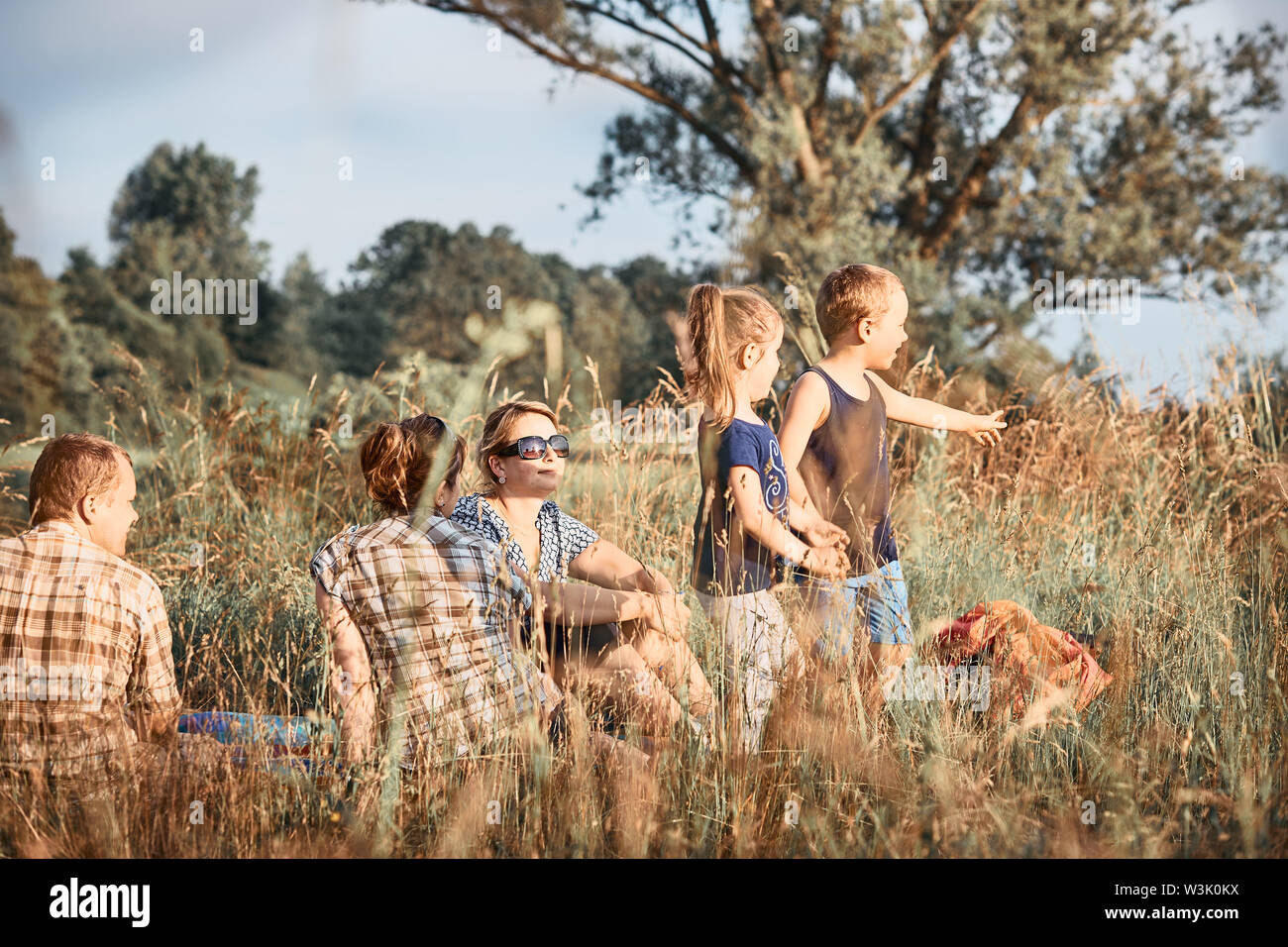 Family spending time together on a meadow, close to nature. Parents and children sitting and playing on a blanket on grass. Candid people, real moment Stock Photo