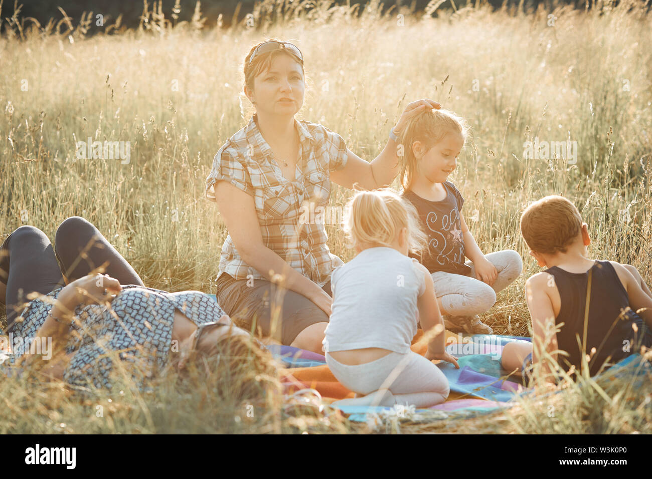 Family spending time together on a meadow, close to nature. Parents and children sitting and playing on a blanket on grass. Candid people, real moment Stock Photo