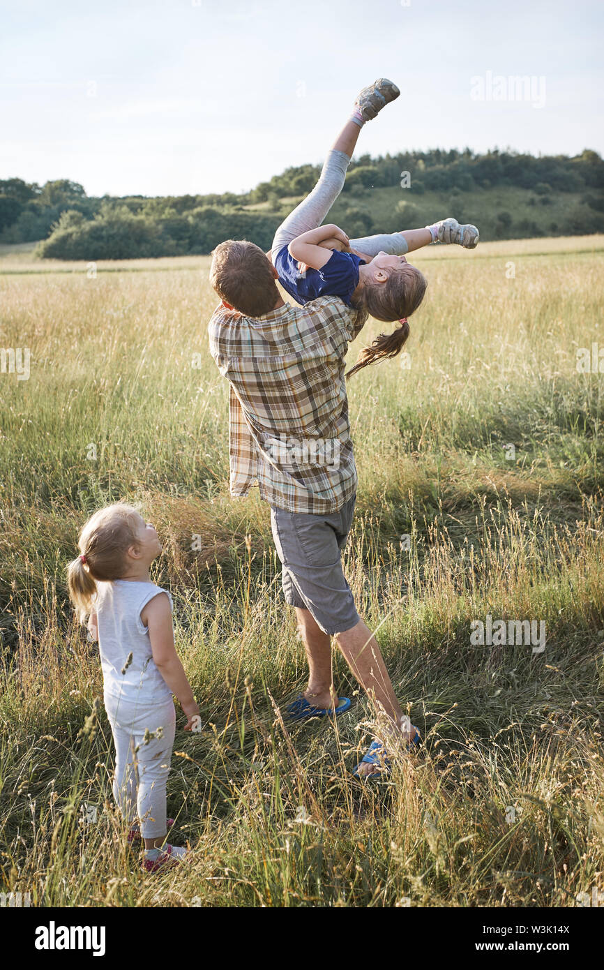 Father tossing little girl in the air. Family spending time together on a meadow, close to nature. Parents and children playing together. Candid peopl Stock Photo