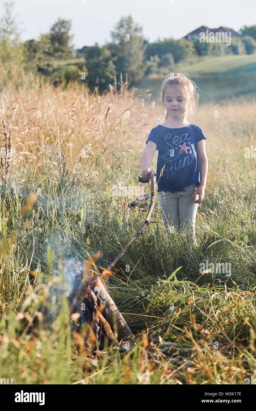 Little girl roasting marshmallow over a campfire on a meadow. Candid people, real moments, authentic situations Stock Photo