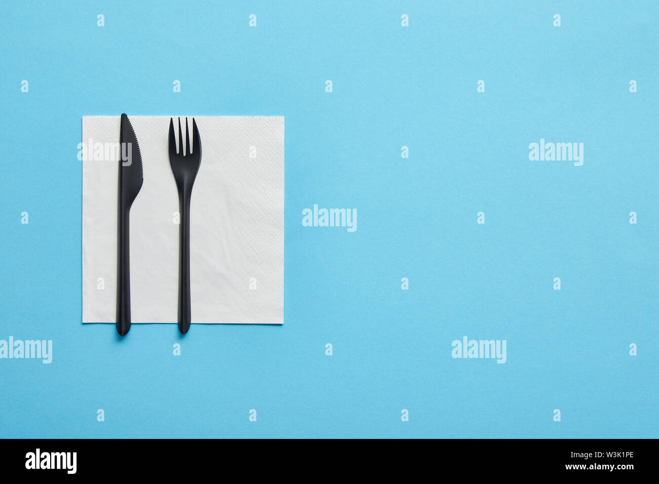Top view of disposable fork and knife lying on napkin on blue background Stock Photo