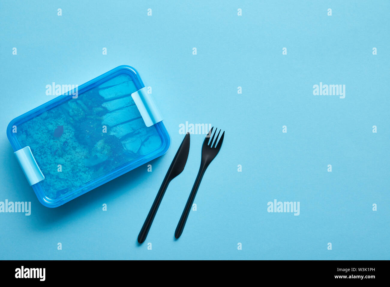 Top view of lunch box with healthy food and disposable fork and knife on blue background Stock Photo