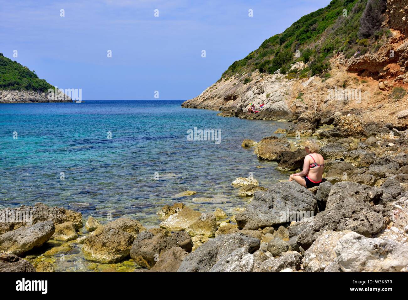 A woman sitting on some rocks,Porto timoni, Cape Arillas, Afionas, Corfu, Greece,ionian islands Stock Photo