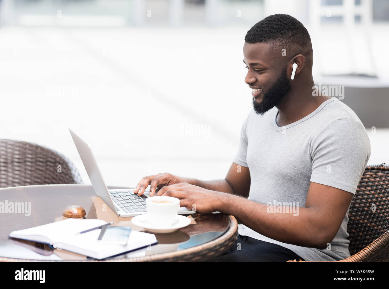 African guy using laptop, smiling and drinking morning coffee Stock Photo