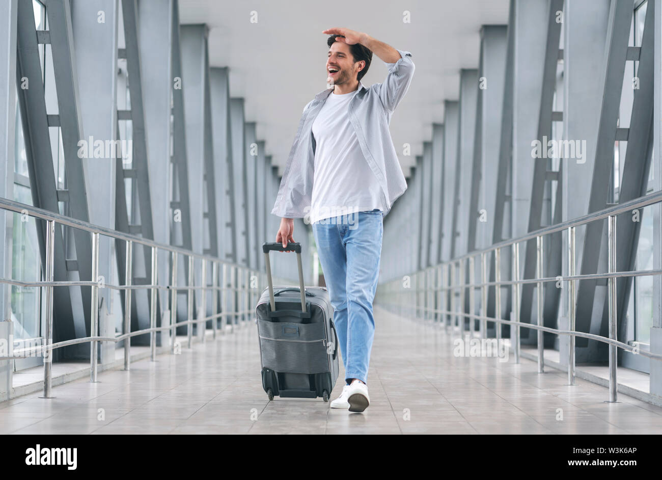 Cheerful man walking with luggage at airport Stock Photo - Alamy