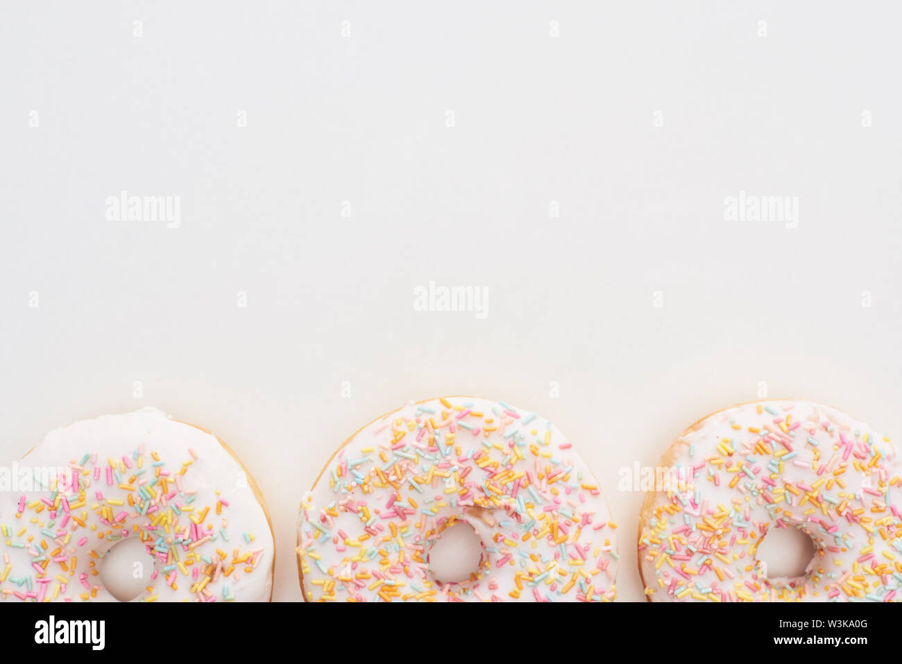 top view of white glazed doughnuts with sprinkles on white background ...