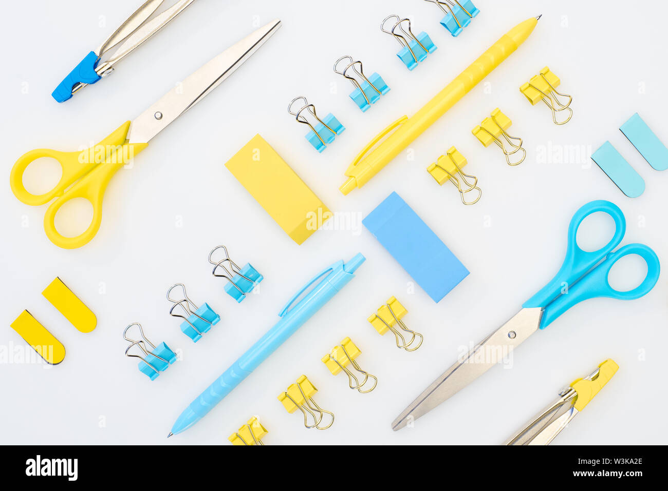 flat lay of yellow and blue erasers, pens, scissors, compasses and paper clips isolated on white Stock Photo