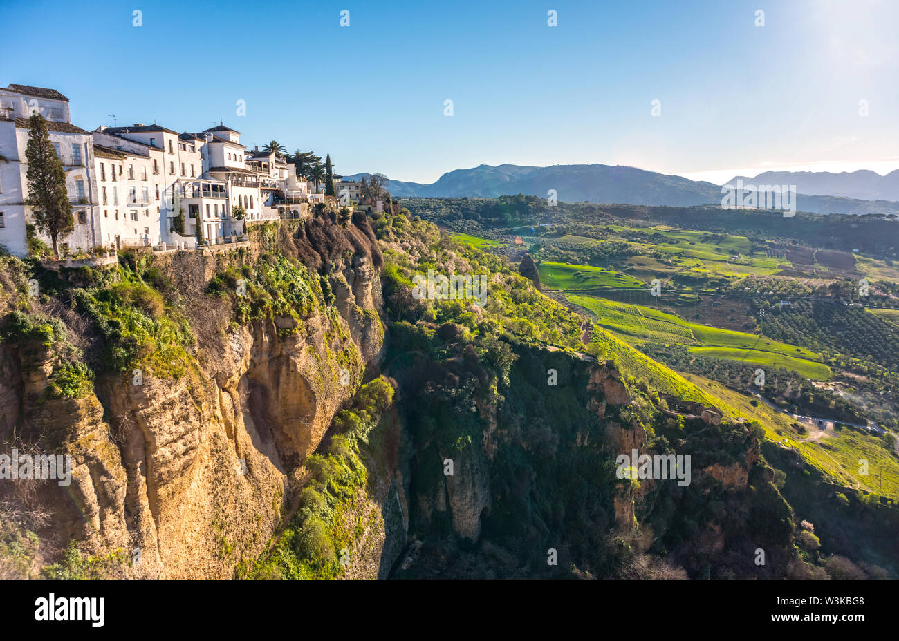 Ronda, Spain: Landscape of white houses on the green edges of steep cliffs with mountains in the background. Stock Photo