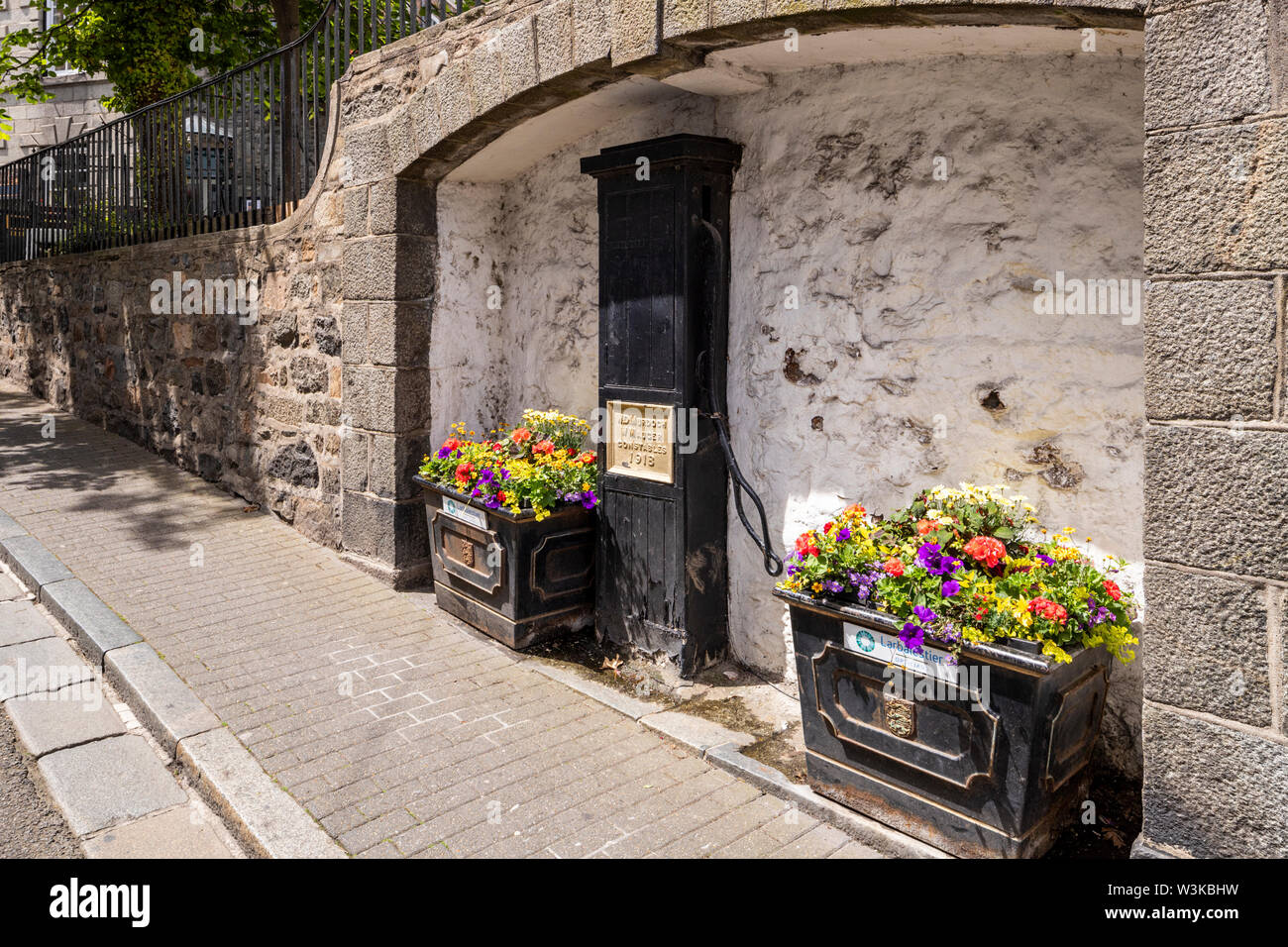 Floral displays beside an old public water pump dated 1918 in The Pollett under La Plaiderie, St Peter Port, Guernsey, Channel Islands UK Stock Photo