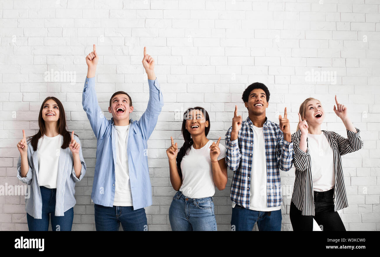 Teens pointing up on free space over white brick wall Stock Photo