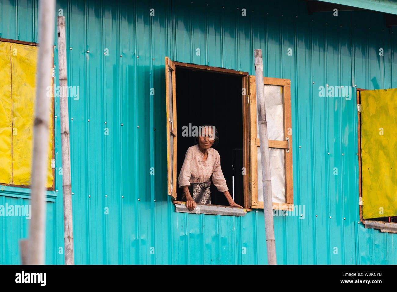 Maing Thauk, Myanmar - April 2019: old Burmese woman looking out of the floating house window. Stock Photo