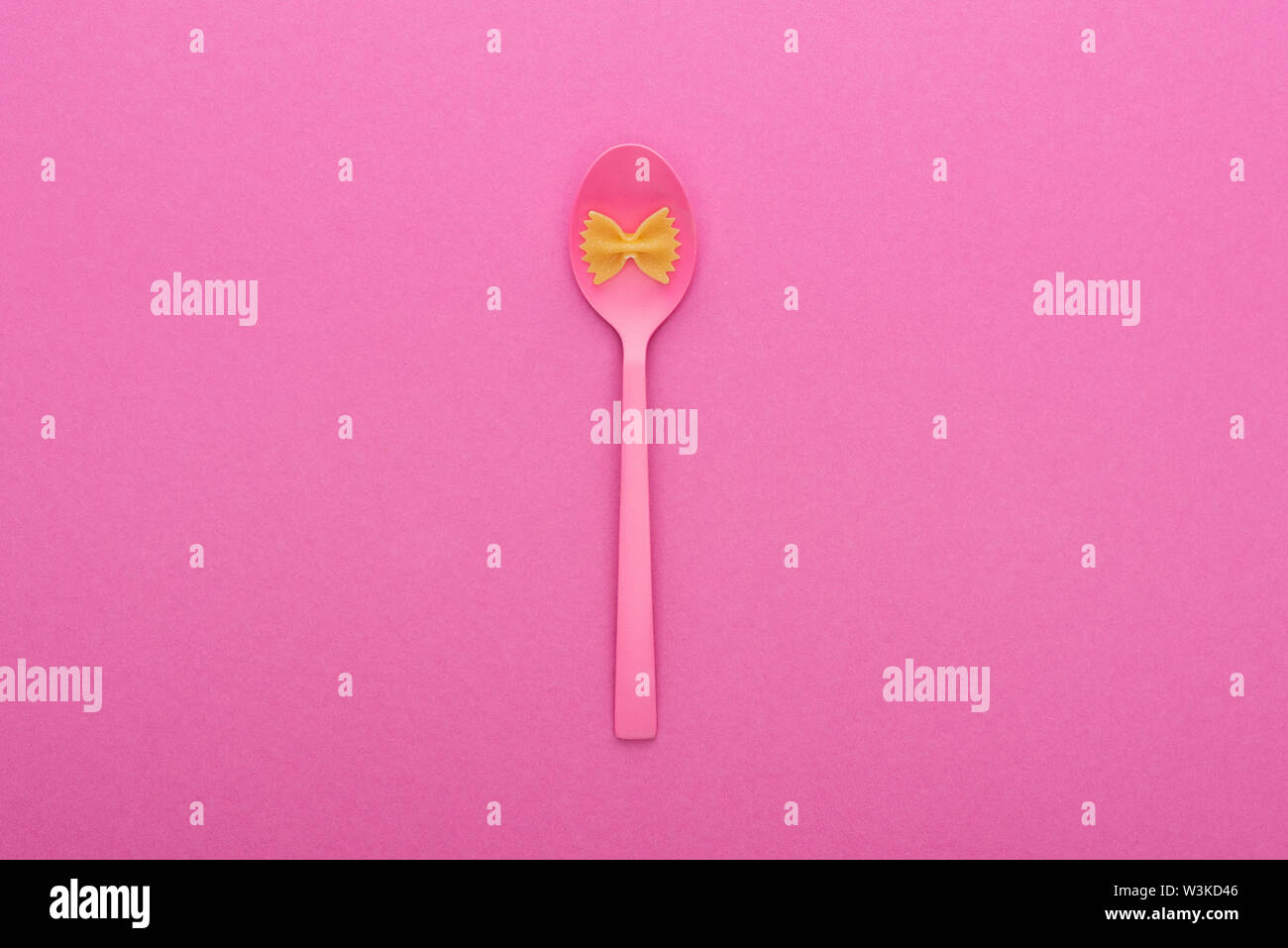 uncooked farfalle pasta on plastic spoon bowl isolated on pink Stock Photo