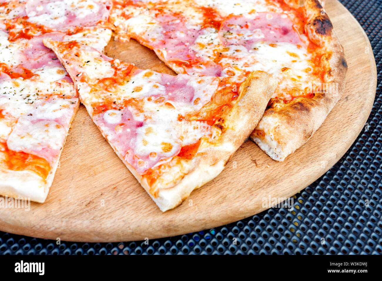 Ham and cheese pizza on a wooden platter with a slice cut out Stock