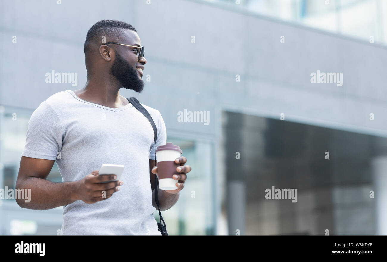 Young african man with phone and coffee to go enjoying day Stock Photo