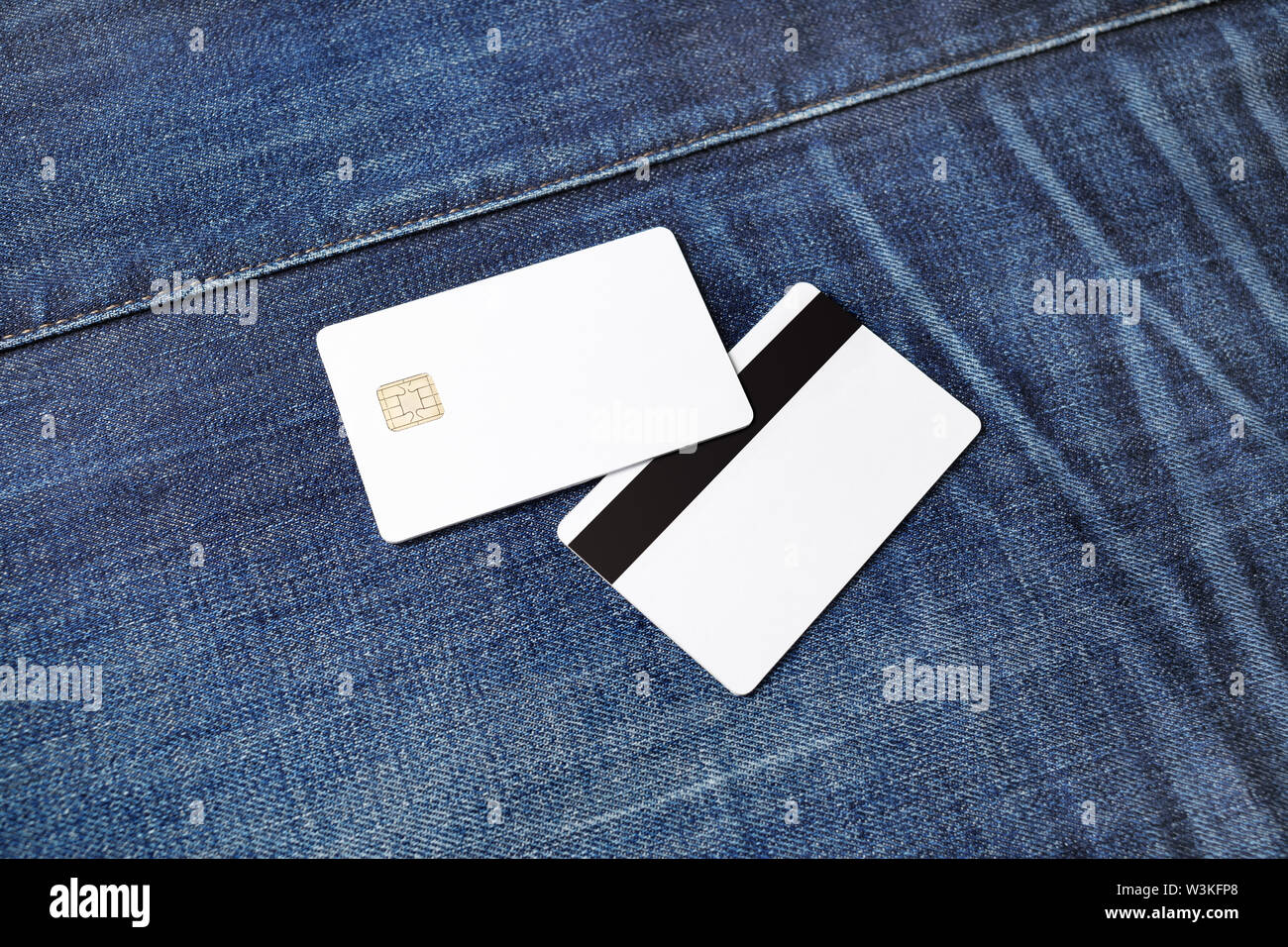 Two bank plastic bank cards on denim background. White credit cards. Front and back view. Stock Photo