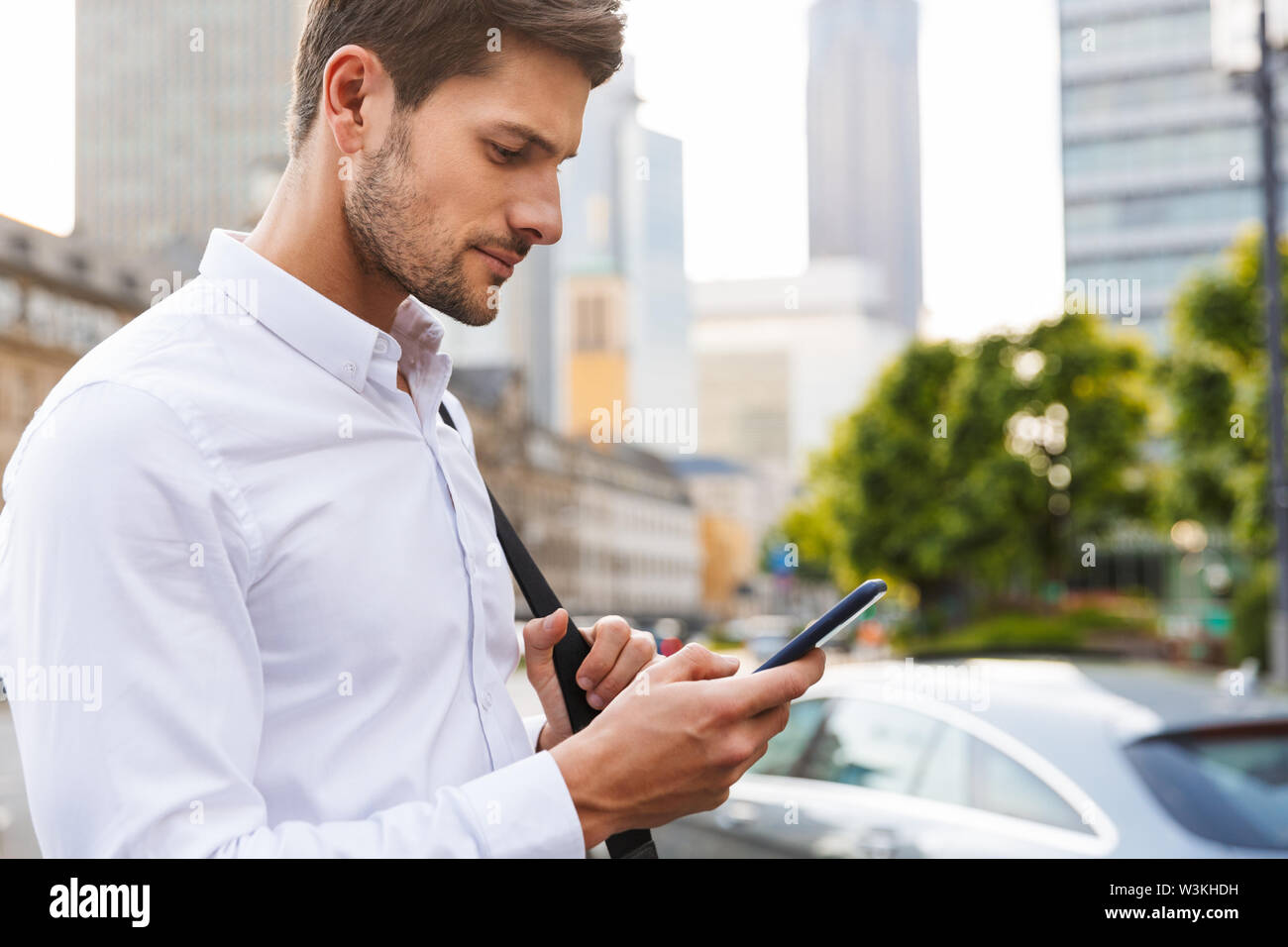 Image of a serious young businessman walking by street using mobile phone chatting. Stock Photo
