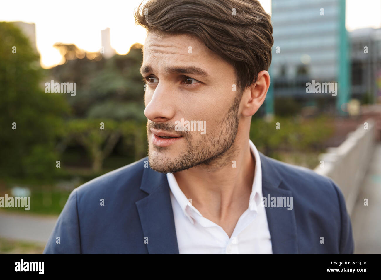 Photo of a young serious concentrated unshaved businessman outdoors on the street looking aside. Stock Photo