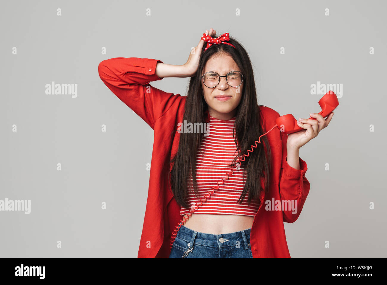 Cute upset teenage girl wearing casual outfit standing isolated over gray background, calling on landline phone Stock Photo