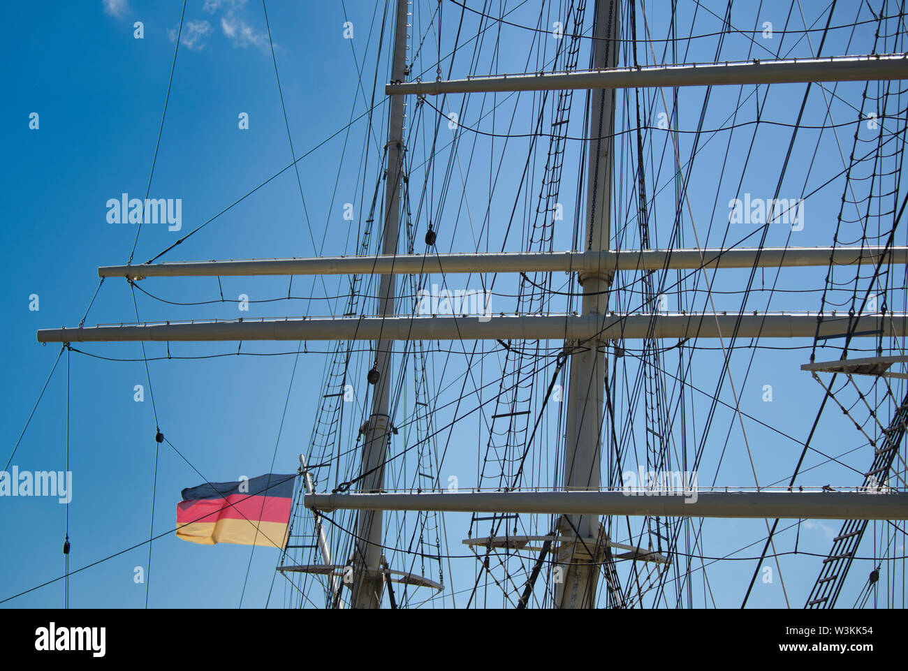 rigging and masts of a big sailing ship in front of a blue sky with the black-red-golden flag of the state Germany Stock Photo