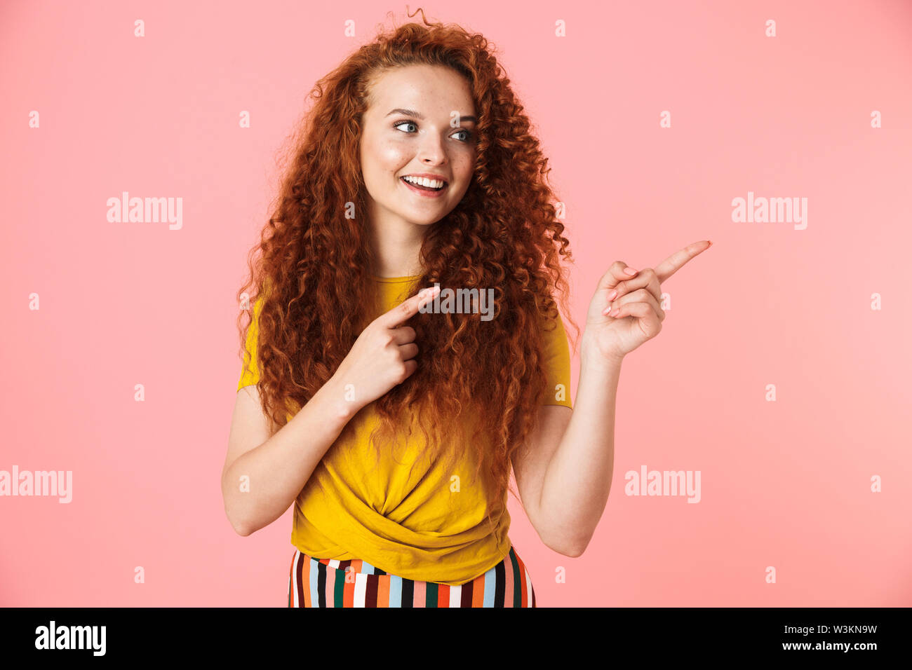 Portrait of an attractive smiling young woman with long curly red hair ...