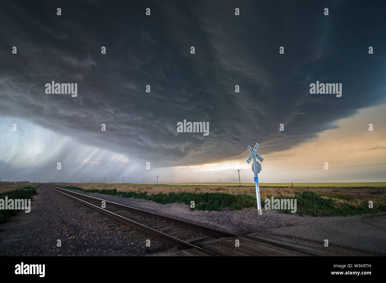 A large storm blows in over a railroad crossing, dumping heavy rain and producing extreme winds. Stock Photo
