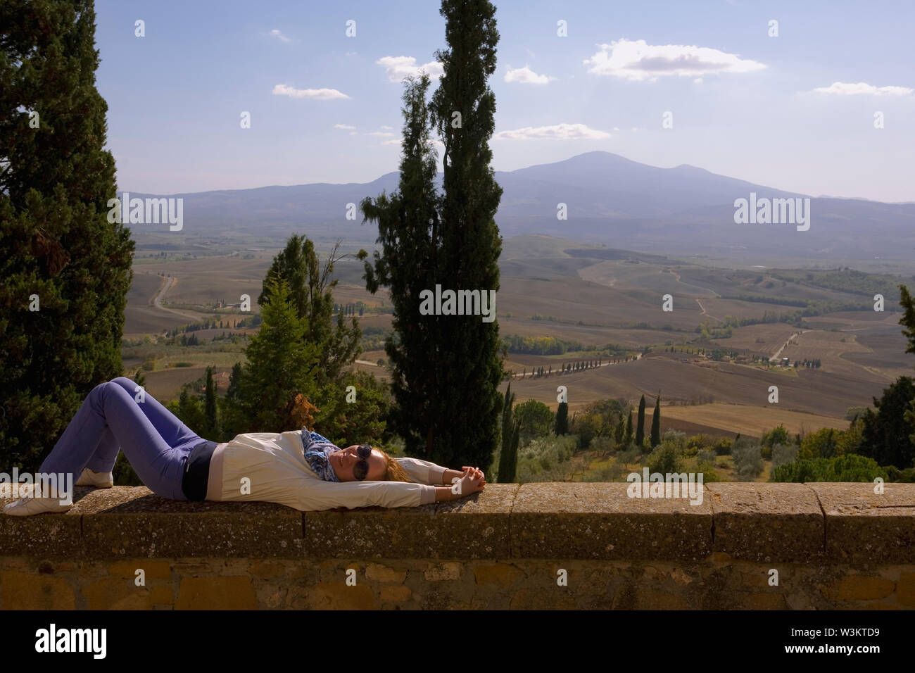 A girl rests on the parapet of Via Gozzante, on the Passeggiata Panoramica, Pienza, with a wide view over the Val d'Orcia to Monte Amiata Stock Photo