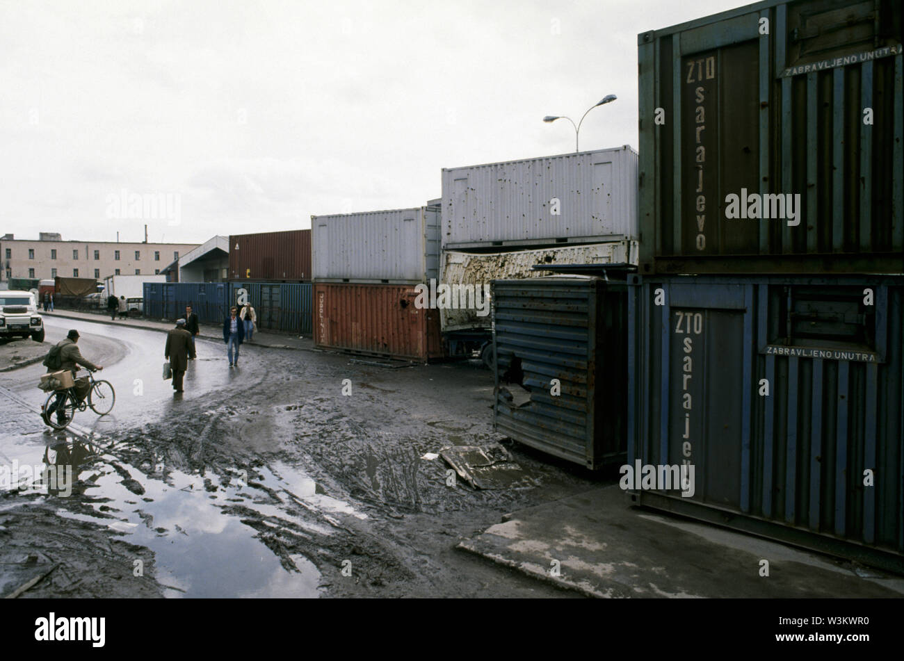 11th April 1993 During the Siege of Sarajevo: local people walk past shrapnel-ridden containers that act as a sniper screen across Hamdije Cemerlica at the junction with Put zivota (known as Bratstva i jedinstva and Krusevacka during the war). Stock Photo