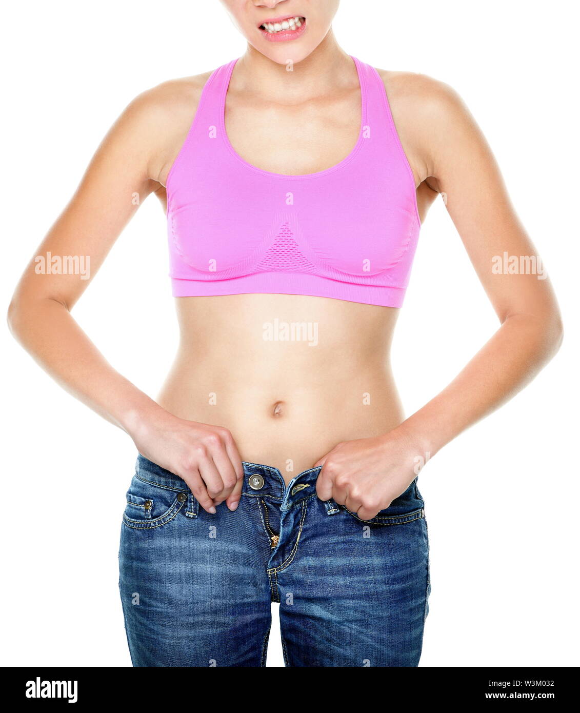 Weight gain and weight loss woman buttoning pants with difficulties. Jeans  too tight on female waist. Woman making funny face expression isolated on  white background. Mixed race Asian Caucasian model Stock Photo -