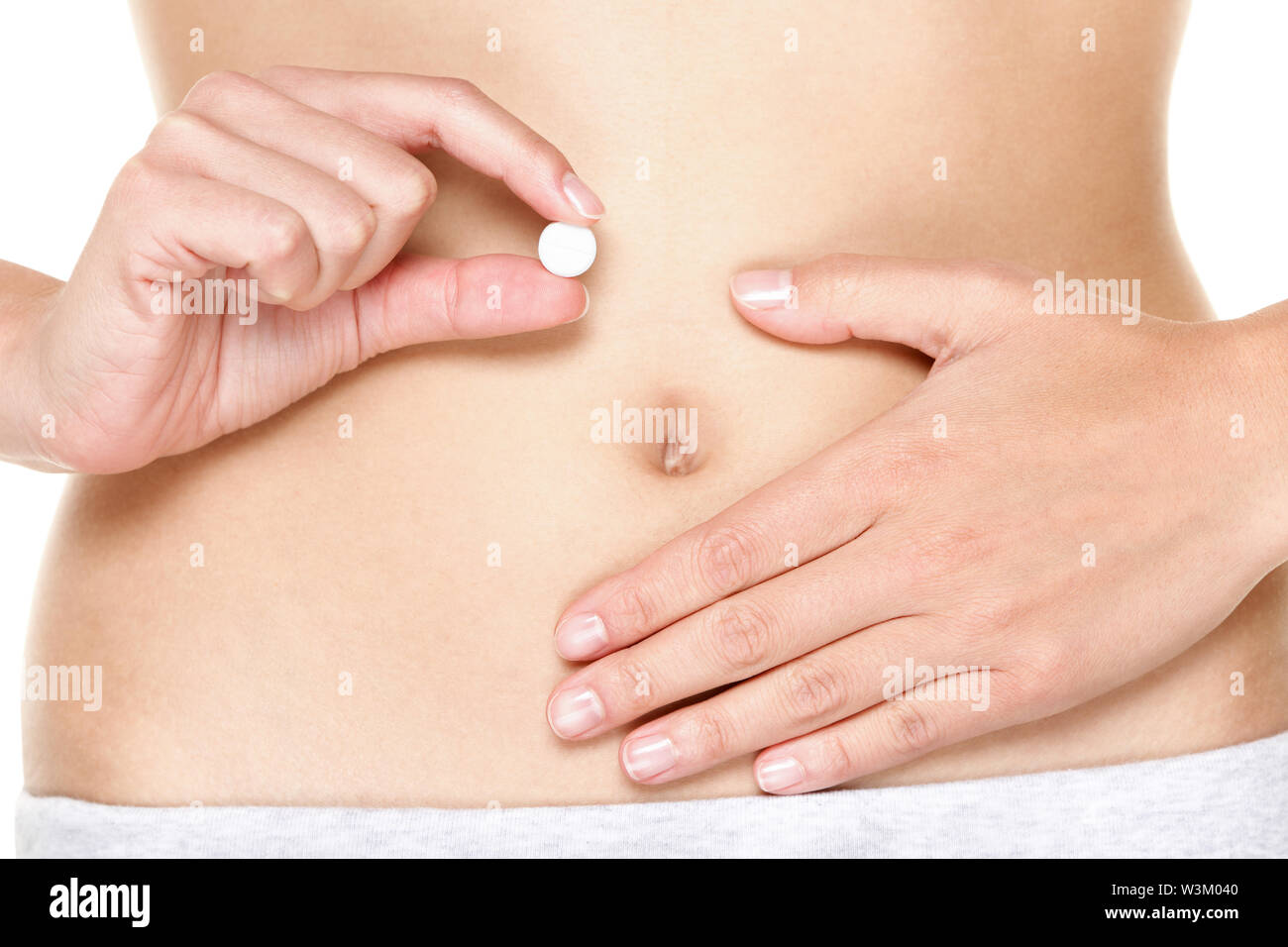Birth control pill, Contraceptive pills, Vitamin pill, pills for better digestion or pills against menstrual pain. Woman holding white tablet in front of stomach. Close up. Stock Photo