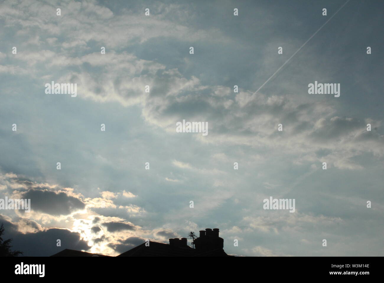 Sun rays coming through dark clouds onto bright blue sky Stock Photo