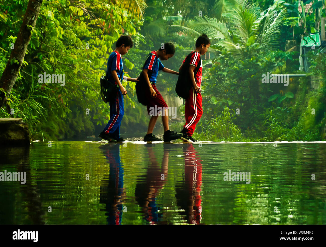 boy crossing stream water going to school in rural area Stock Photo