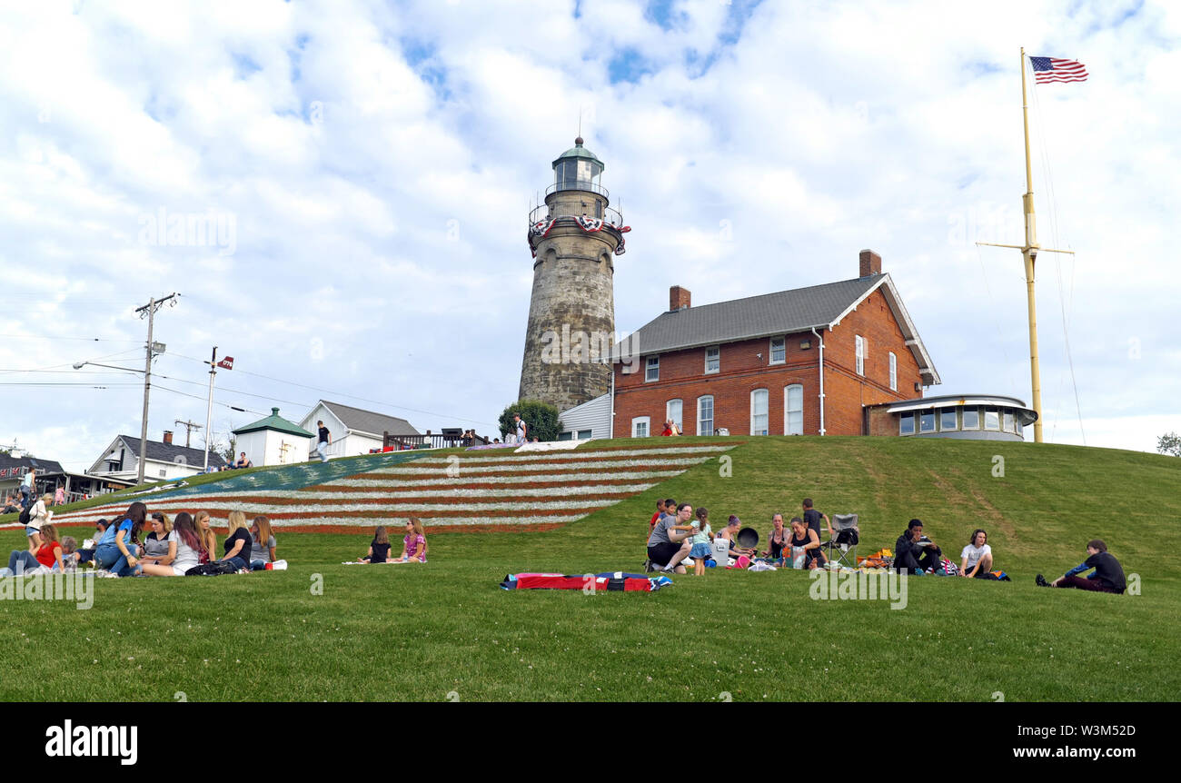 Americans on July 4th weekend relax near the Fairport Harbour lighthouse and the giant grass US flag in Fairport Harbour, Ohio, USA. Stock Photo