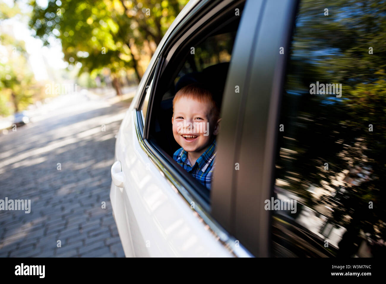 Adorable baby boy in the car. Laughing boy looks out of the car window. Stock Photo