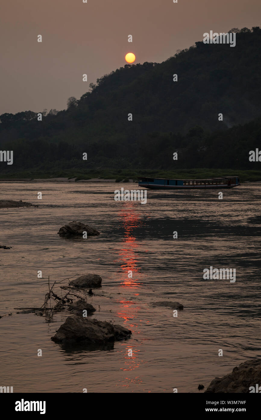 View of a river cruise ship on the Mekong River and Chomphet District across the river in Luang Prabang, Laos, at sunset. Stock Photo