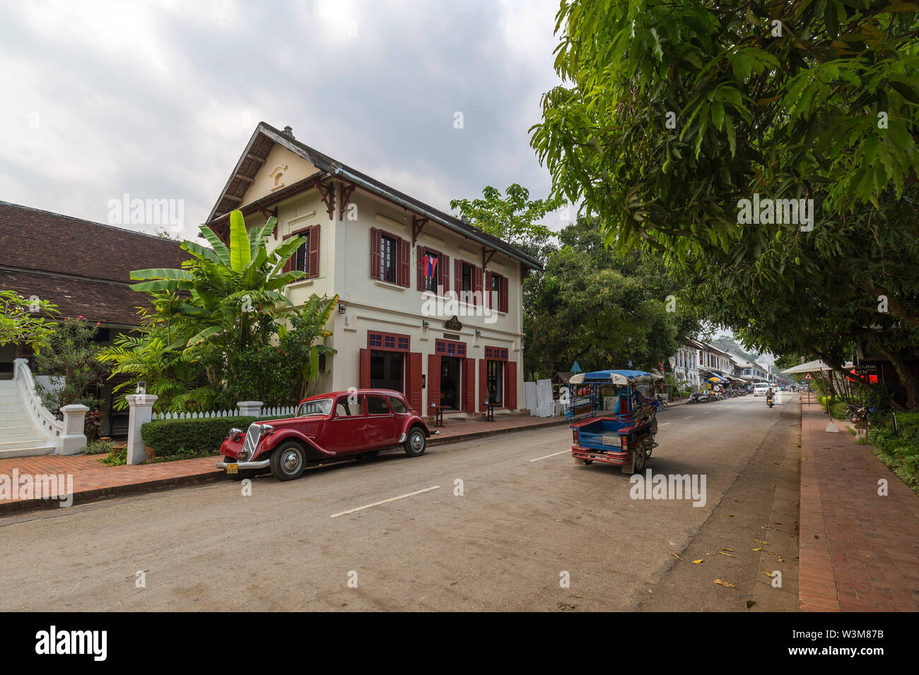 Old Citroen car parked in front of an old French colonial building and little traffic on the idyllic Sakkaline Road in Luang Prabang in the morning. Stock Photo