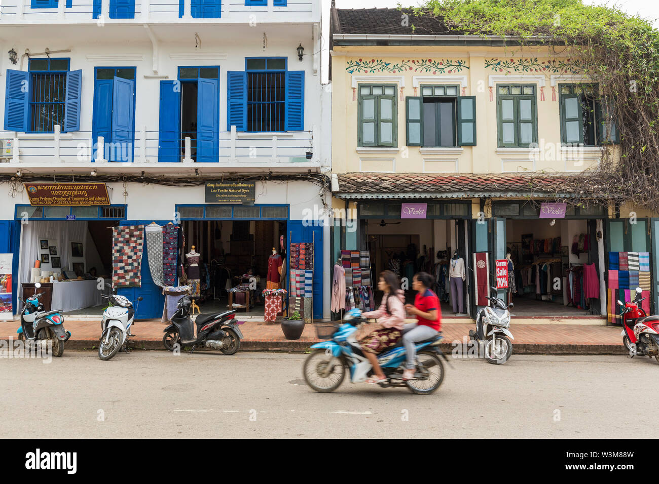 Women on scooter passing old French colonial era buildings on the Kingkitssarath Road in Luang Prabang, Laos. Stock Photo