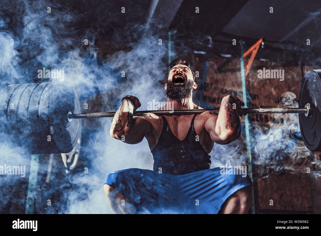 Muscular bearded tattoed fitness man doing deadlift a barbell over his head in modern fitness center. Functional training. Snatch exercise Stock Photo