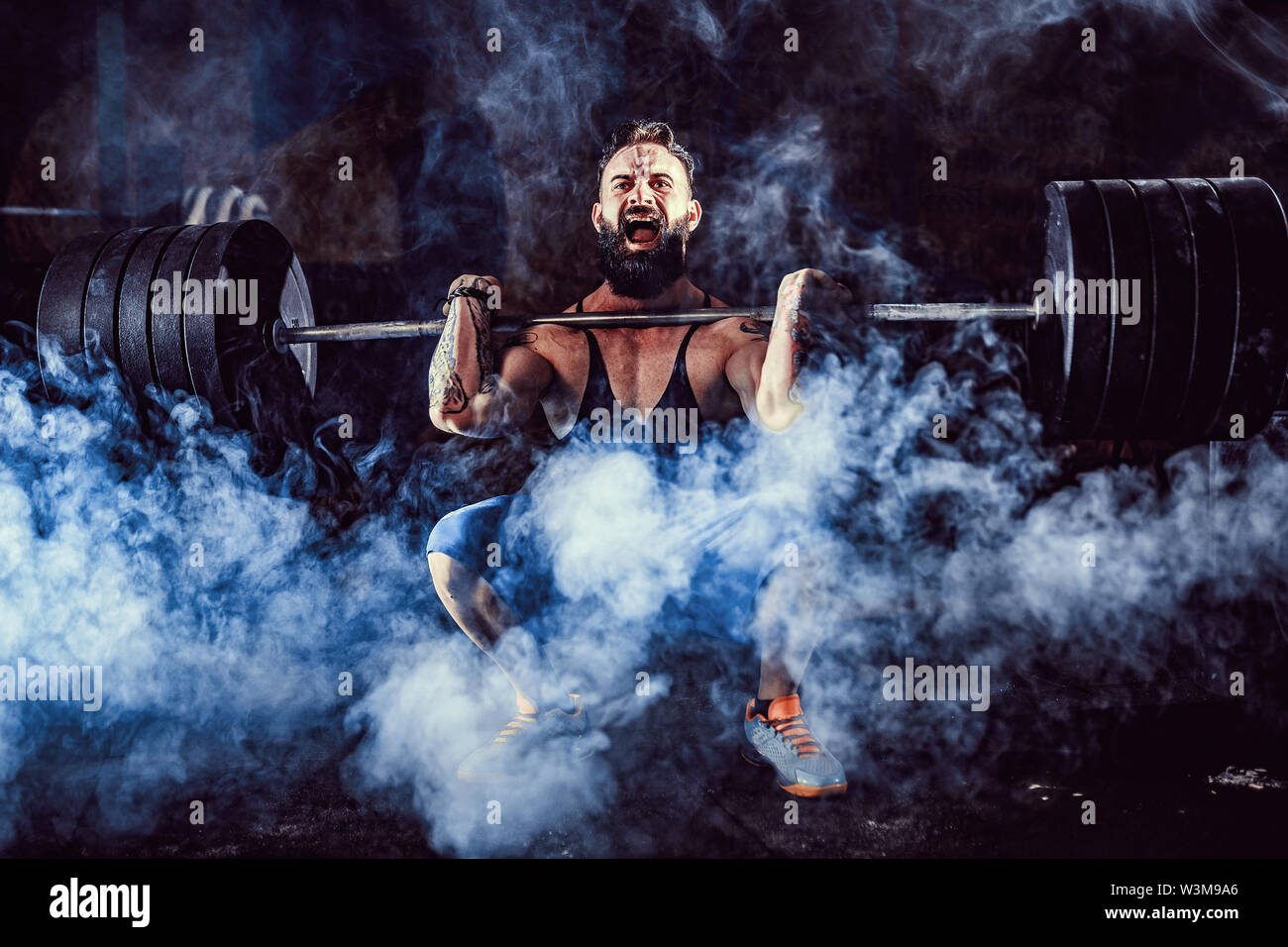 Muscular bearded tattoed fitness man doing deadlift a barbell over his head in modern fitness center. Functional training. Snatch exercise Stock Photo