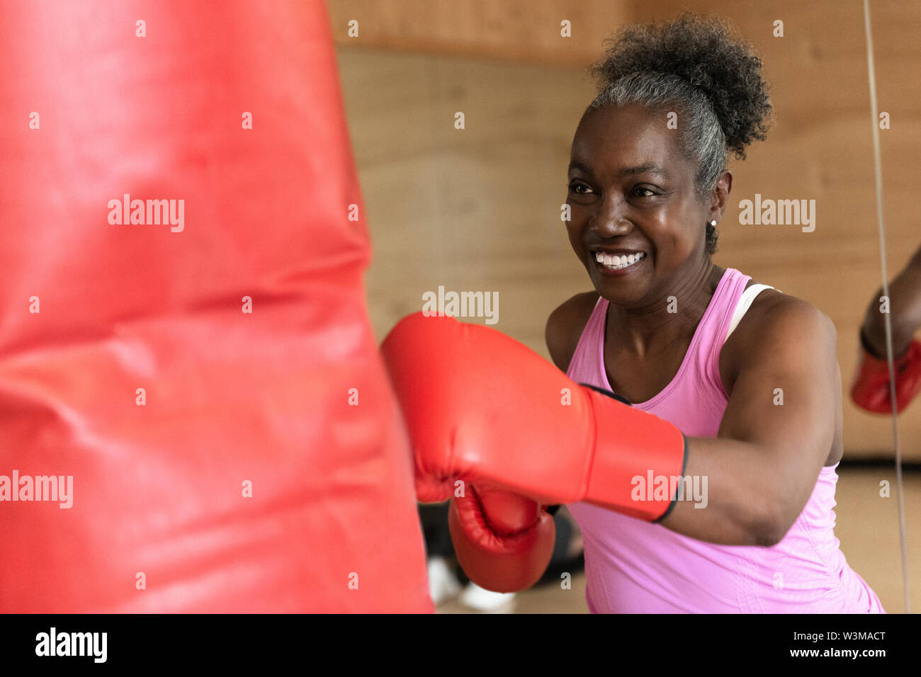Smiling mature woman boxing with punching bag Stock Photo - Alamy